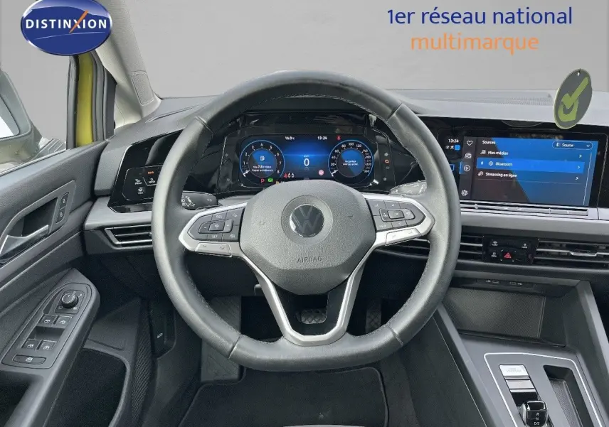 Vue intérieure centrée sur le volant et le tableau de bord numérique d'une Volkswagen Golf jaune 2020.