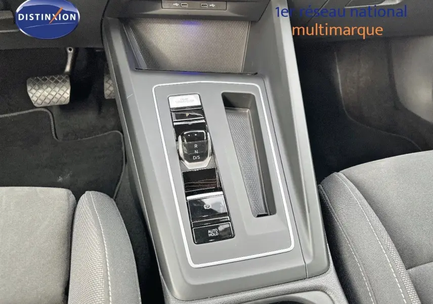 Vue rapprochée de la console centrale grise avec levier de vitesse automatique et sièges tissu gris d'une Volkswagen Golf jaune.