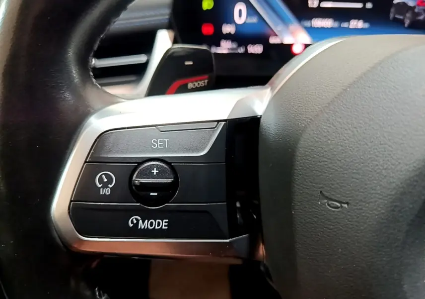 Gros plan sur le volant cuir noir de la BMW X1 xDrive23i M Sport, avec commandes de régulateur de vitesse et affichage digital en arrière-plan.