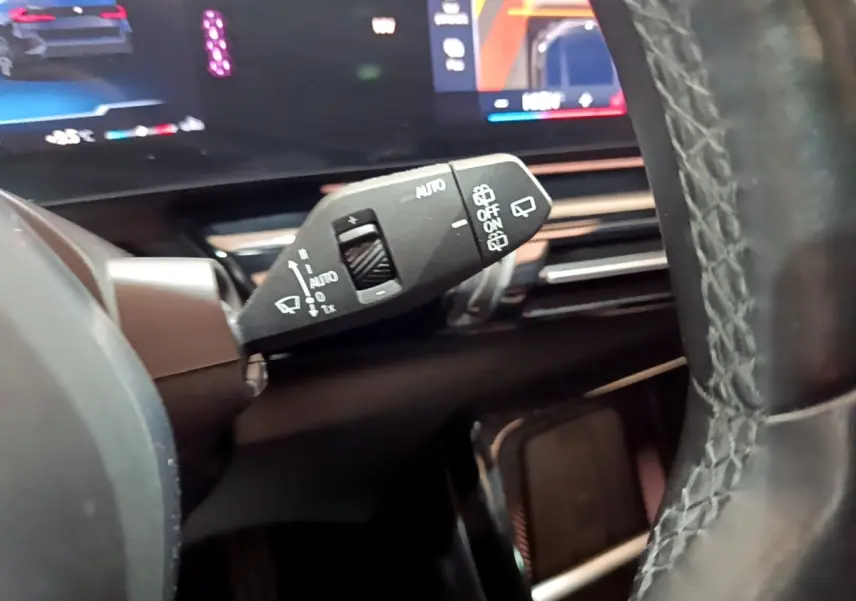 Gros plan sur la commande d’essuie-glace à gauche du volant cuir noir dans l’habitacle d’un BMW X1 noir 2023.