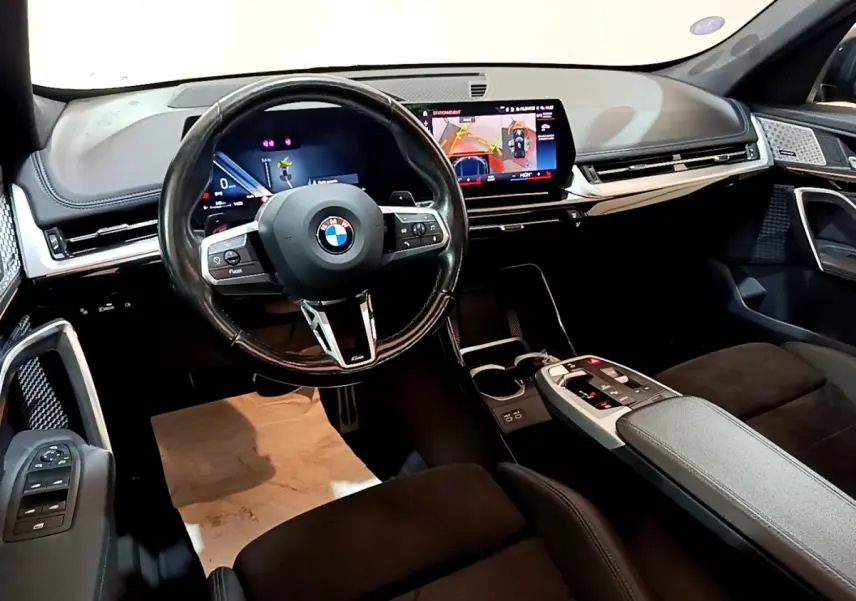 Intérieur BMW X1 xDrive23i M Sport 2023 vu côté conducteur, tableau de bord noir avec écran tactile et volant cuir alu.
