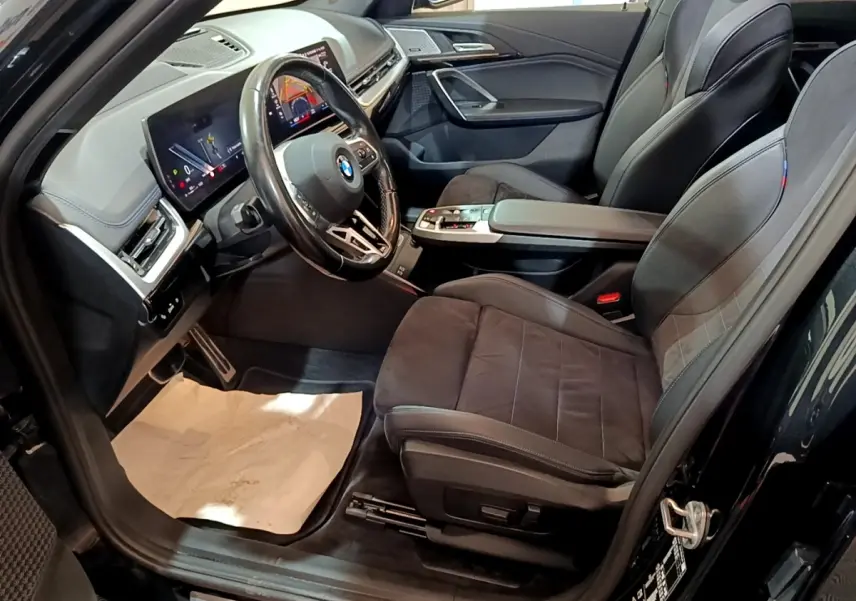 Vue intérieure côté conducteur du BMW X1 xDrive23i M Sport 2023 noir, avec sièges sport et tableau de bord digital.