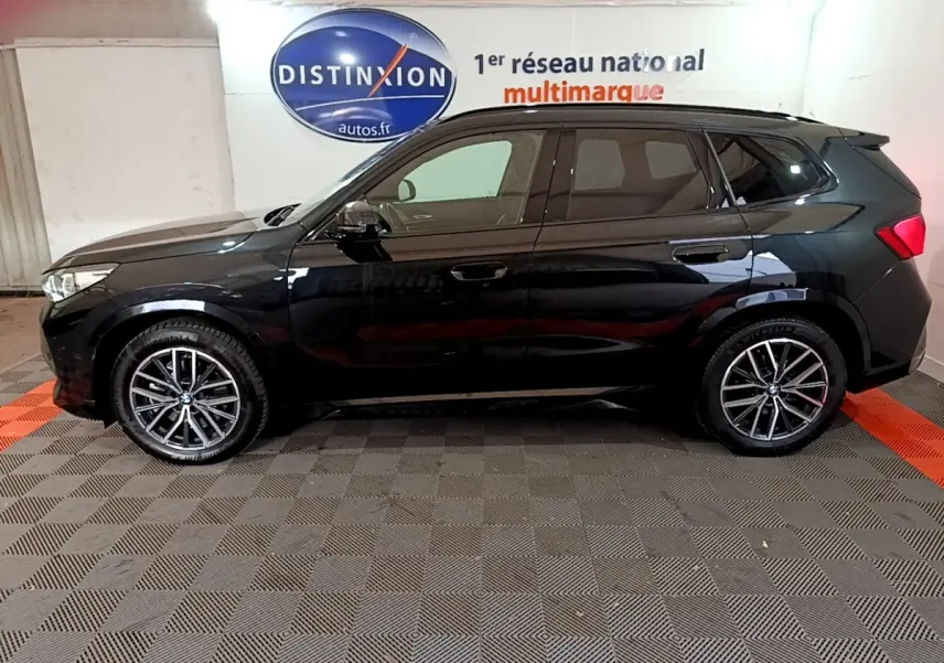 BMW X1 xDrive23i M Sport noir vue de profil côté gauche, jantes alliage et logo Distinxion en arrière-plan.