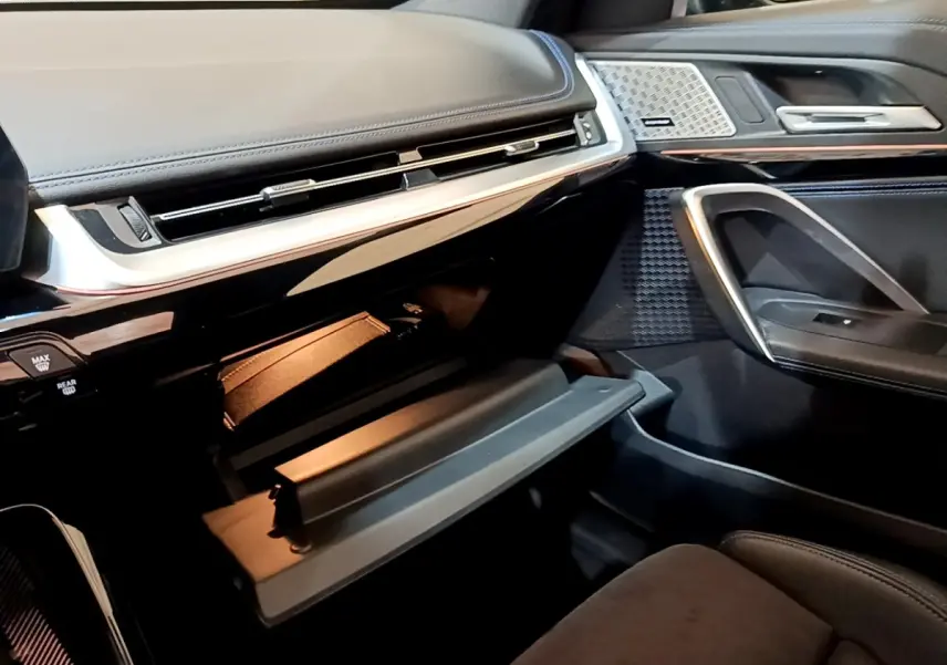 Intérieur BMW X1 xDrive23i M Sport 2023, vue côté passager sur boîte à gants ouverte et tableau de bord noir.