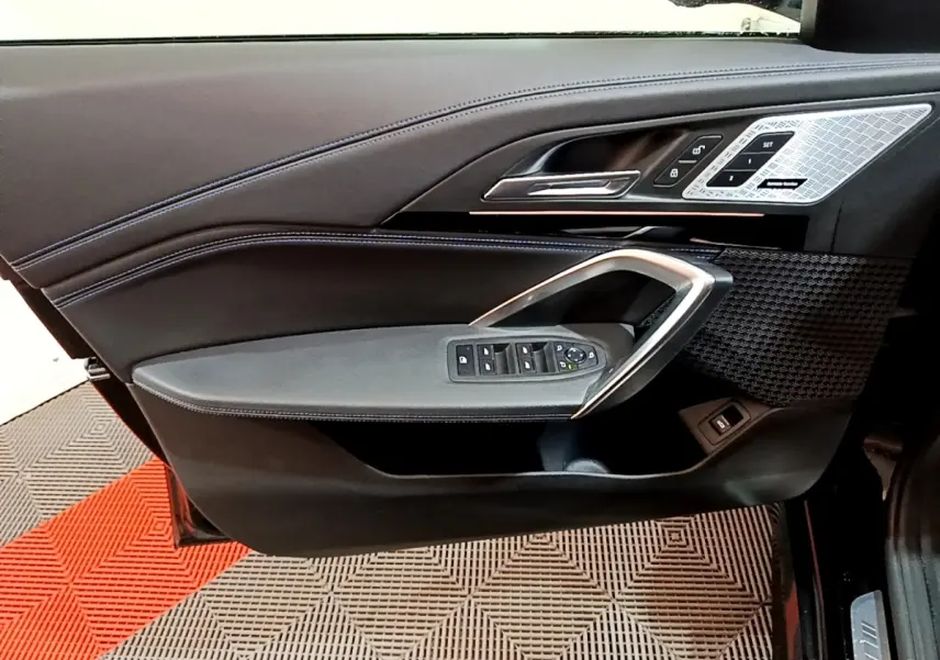 Vue latérale du panneau de porte conducteur noir avec commandes vitres et insert décoratif argenté du BMW X1 xDrive23i M Sport 2023.