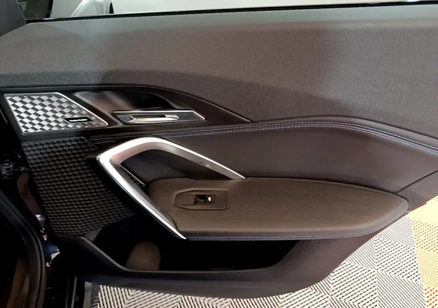 Vue intérieure du panneau de porte côté gauche du BMW X1 xDrive23i M Sport 2023 avec surpiqûres bleues et insert carbone.