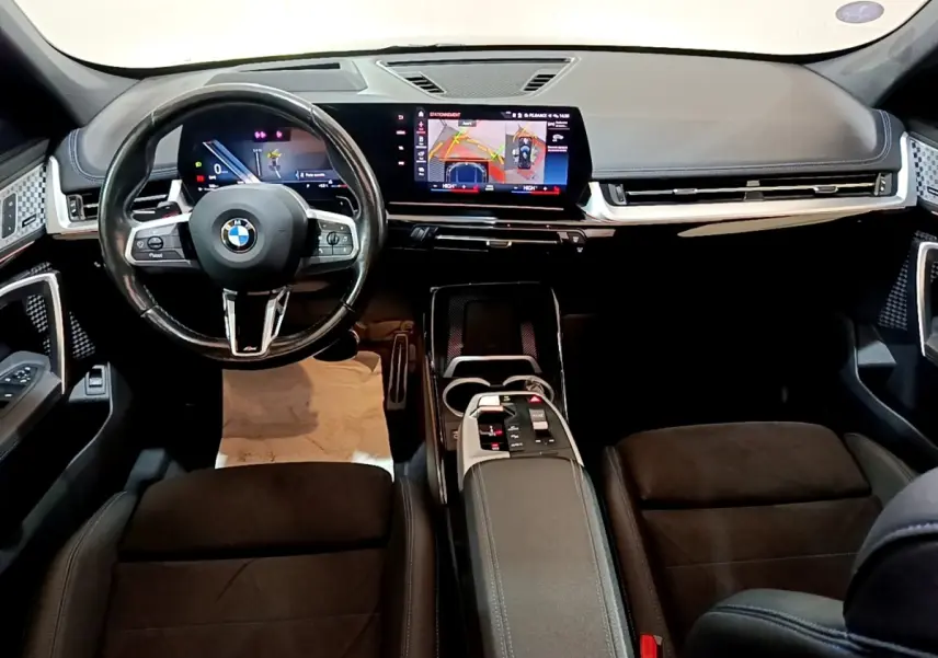 Vue intérieure avant du tableau de bord noir et volant cuir d’une BMW X1 xDrive23i M Sport 2023 avec écran tactile large.