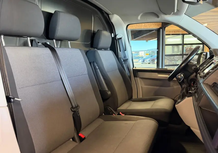 Vue intérieure côté conducteur du Volkswagen Transporter 2019, sièges tissu gris et tableau de bord noir.