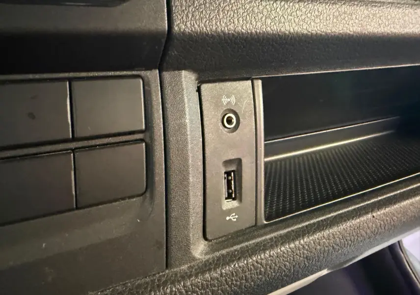 Vue rapprochée du tableau de bord noir du Volkswagen Transporter 2019, montrant une prise USB et une entrée audio auxiliaire.