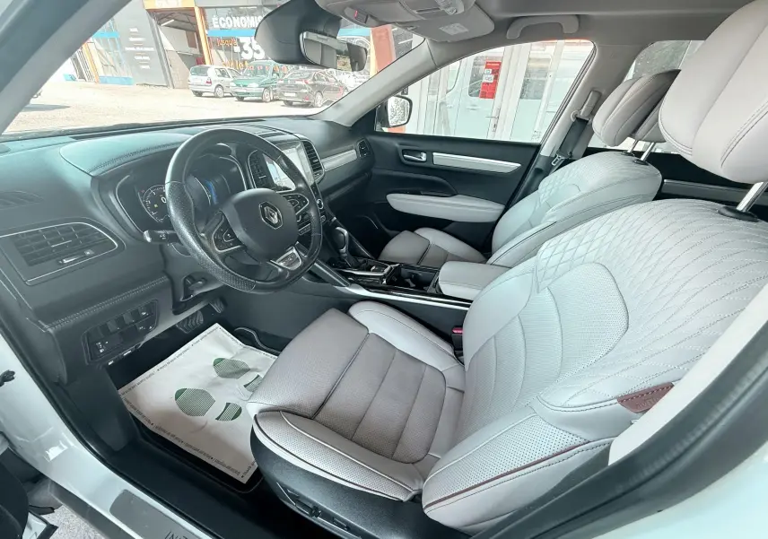 Vue intérieure côté conducteur du Renault Koleos blanc 2021, sièges cuir beige clair avec surpiqûres et tableau de bord noir.