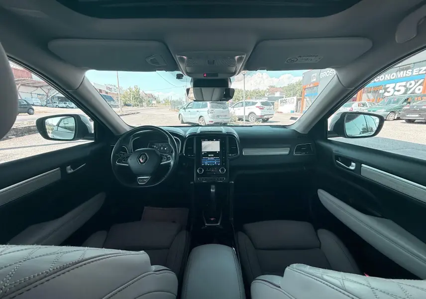 Vue intérieure avant du Renault Koleos blanc 2021, tableau de bord avec écran tactile et volant multifonction noir.