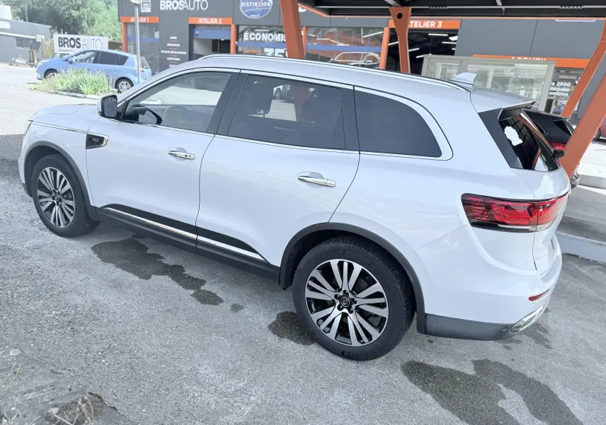 Vue 3/4 arrière droite d'un Renault Koleos blanc garé sous un abri avec jantes alliage et vitres teintées.