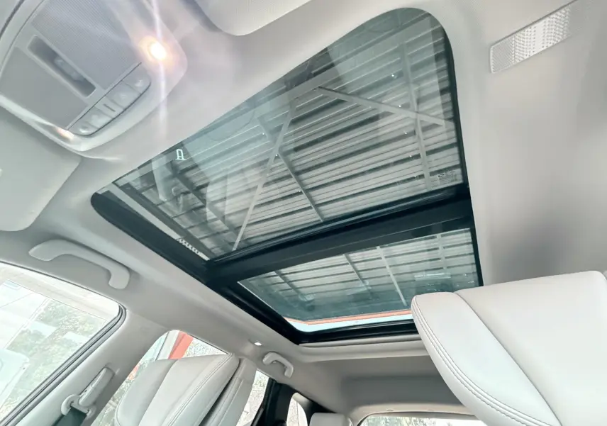 Toit panoramique en verre vu de l'intérieur avant du Renault Koleos blanc, avec sièges avant clairs visibles.