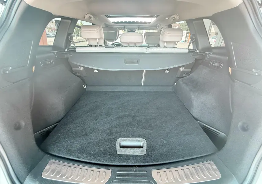 Coffre spacieux vu de l'arrière d'un Renault Koleos blanc, avec cache-bagages et sièges arrière beige visibles.