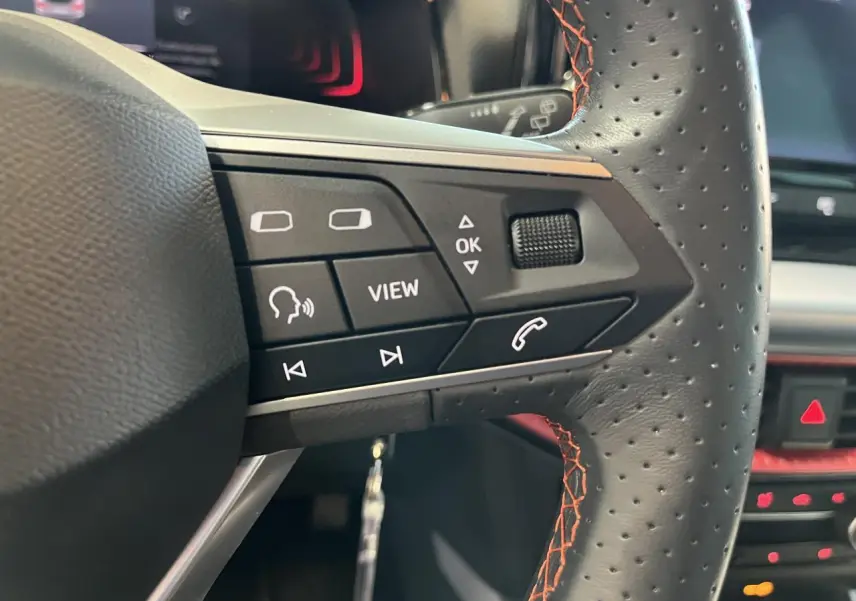 Gros plan sur le volant sport cuir noir avec surpiqûres rouges du SEAT Arona 2024, boutons multifonctions visibles.