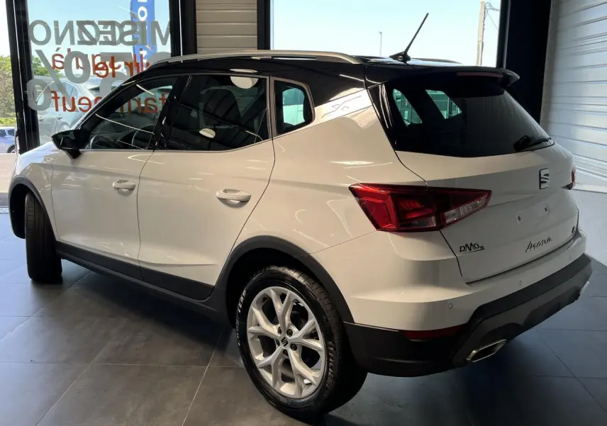 SEAT Arona blanc Nevada vu en 3/4 arrière droit, toit noir et jantes alliage 16 pouces en showroom.