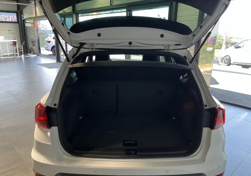 Coffre ouvert vu de l'arrière d'un SEAT ARONA blanc Nevada 2024, intérieur spacieux et tapis noir.