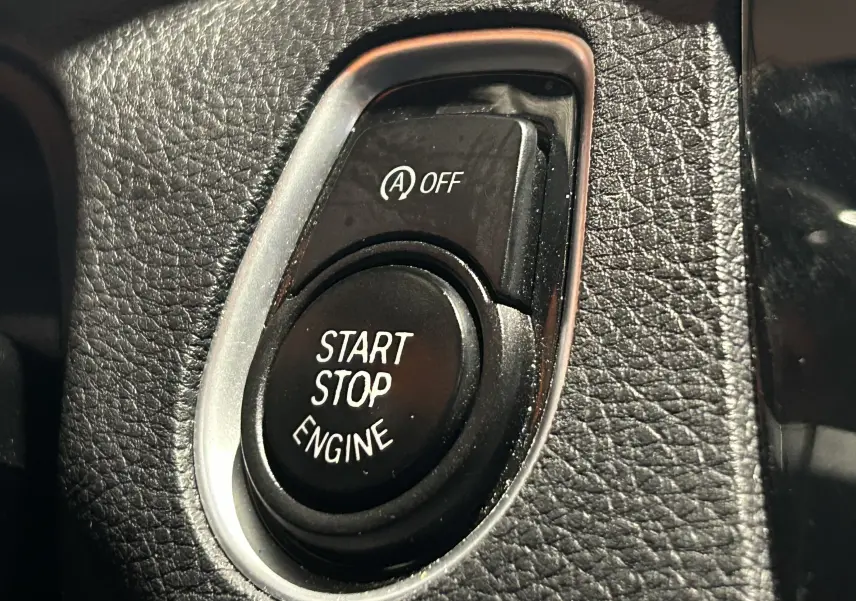 Gros plan sur le bouton Start Stop Engine et la commande Auto Start/Stop désactivée dans l'habitacle d'une BMW Série 1 blanche.