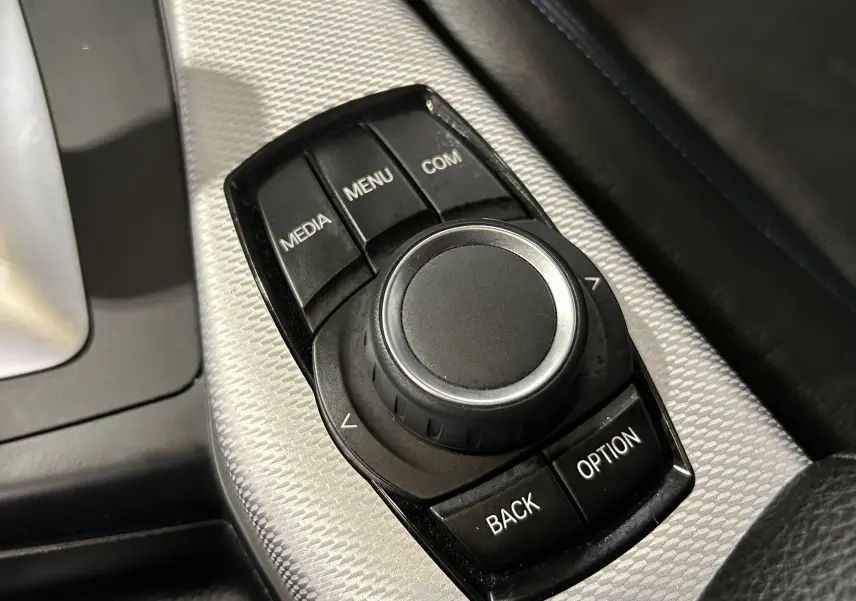 Gros plan sur la molette de commande multimédia noire avec console argentée, intérieur cuir noir BMW Série 1 120iA M Sport 2019.