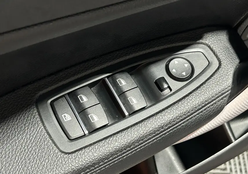 Gros plan sur les commandes de lève-vitres et réglage des rétroviseurs côté conducteur d'une BMW Série 1 blanche 2019 M Sport.