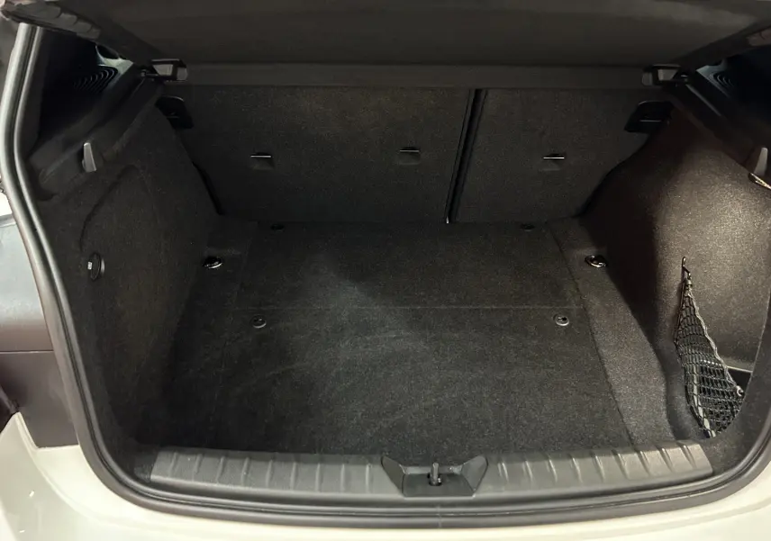 Coffre ouvert vu de l'arrière d'une BMW Série 1 120iA M Sport blanche, espace de chargement vide et tapis noir.