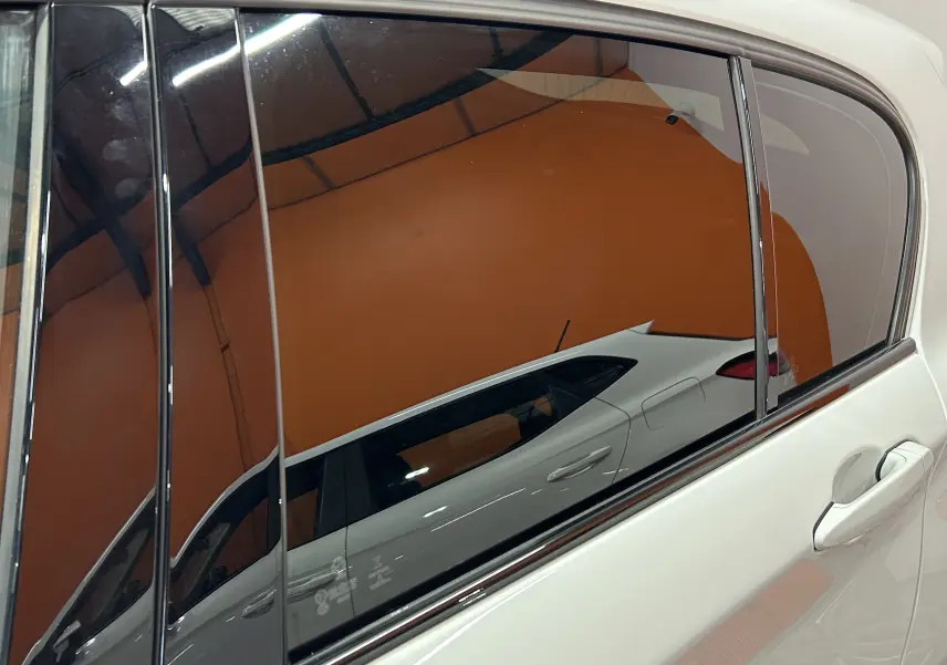 Reflet latéral droit de la BMW Série 1 120iA M Sport blanche, mettant en valeur la porte arrière et la vitre teintée.