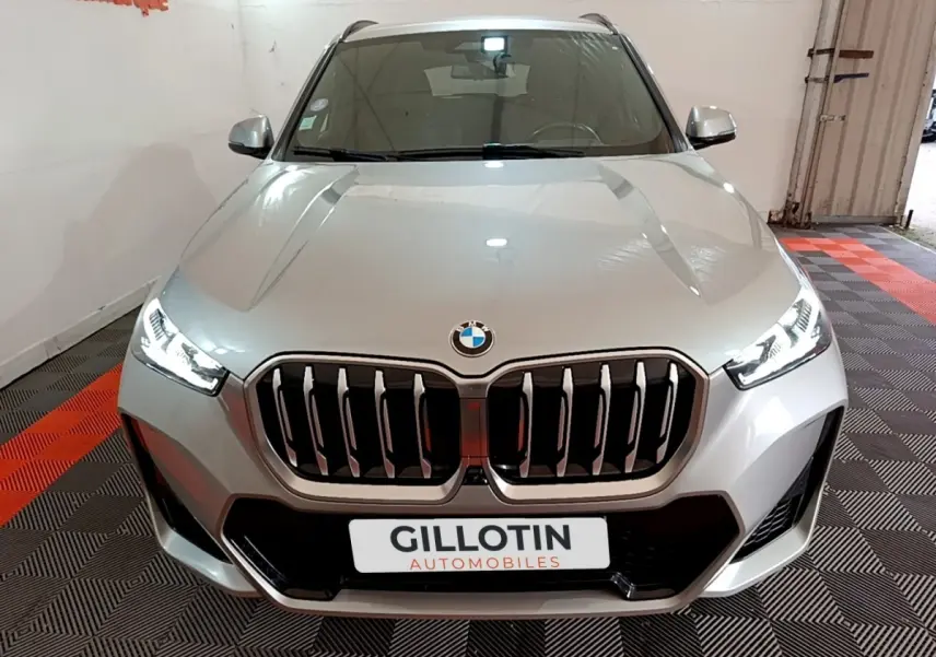 Vue avant d'une BMW X1 xDrive23i M Sport gris clair avec calandre imposante et phares LED allumés.