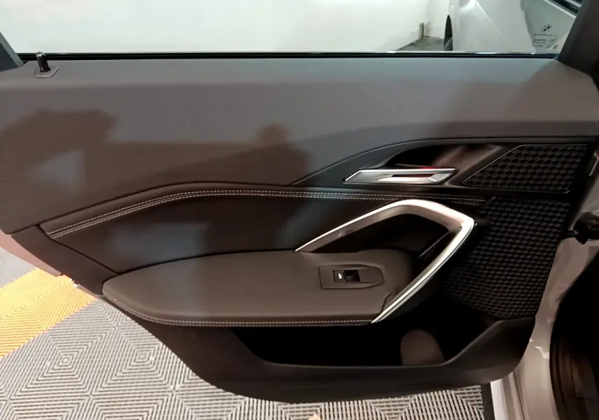 Gros plan sur la porte intérieure côté droit de la BMW X1 gris clair, avec poignée argentée et surpiqûres blanches.