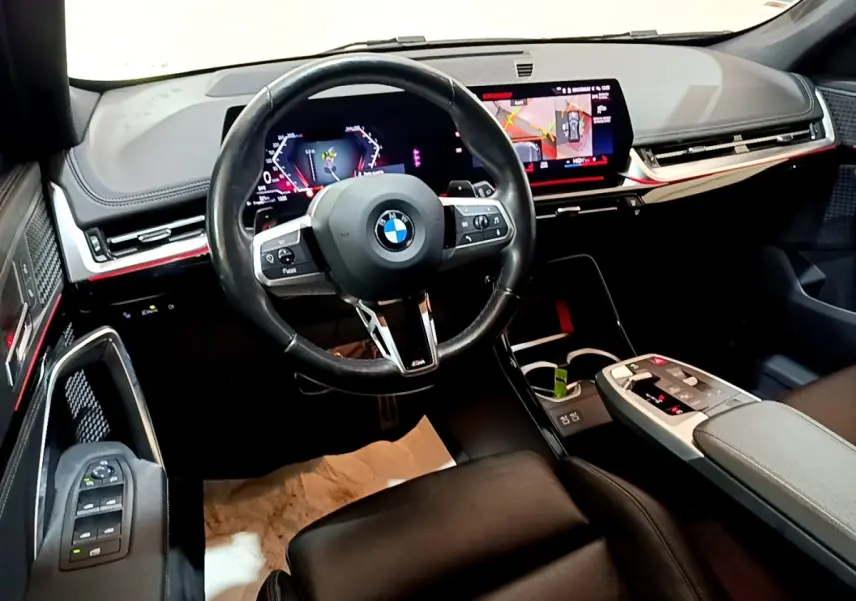 Intérieur BMW X1 xDrive23i M Sport 2023 vu côté conducteur, volant cuir, tableau de bord numérique et écran tactile.