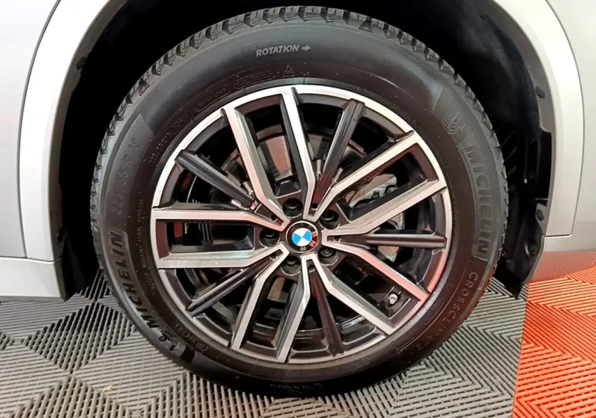 Gros plan sur la roue avant droite d’un BMW X1 gris clair, jante alliage M Sport à design étoilé.