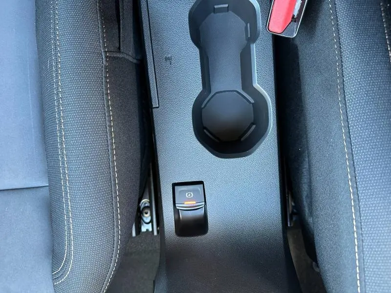 Vue plongeante sur la console centrale noire du Dacia Jogger blanc, avec frein de stationnement électrique et porte-gobelets.