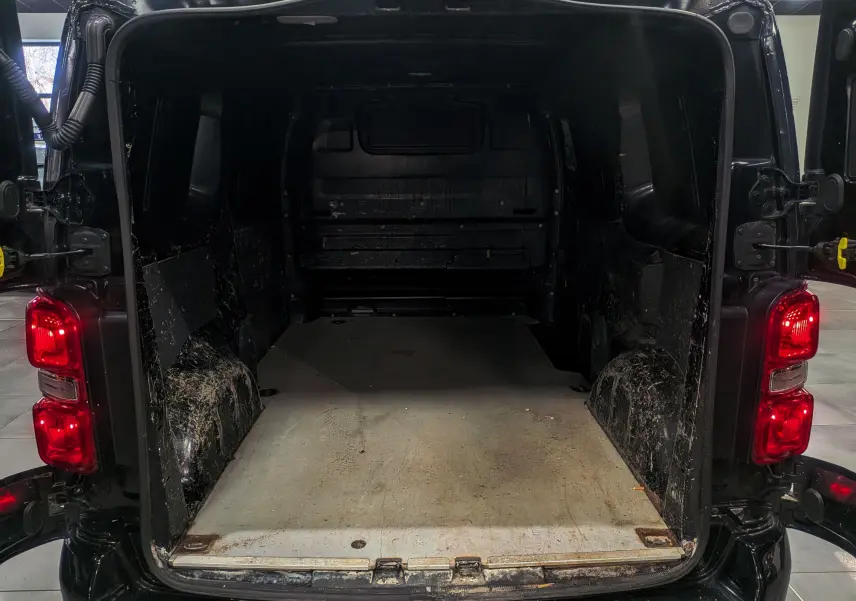 Vue arrière ouverte du Peugeot Expert Fourgon noir Perla, montrant l’espace de chargement vide et les feux arrière allumés.