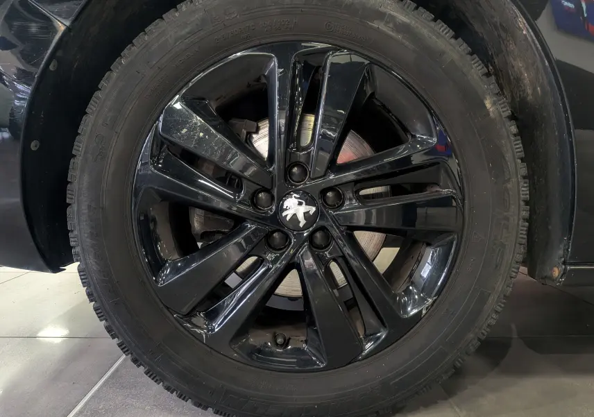 Gros plan sur la jante noire brillante du Peugeot Expert Fourgon noir Perla, mettant en valeur le logo lion au centre.