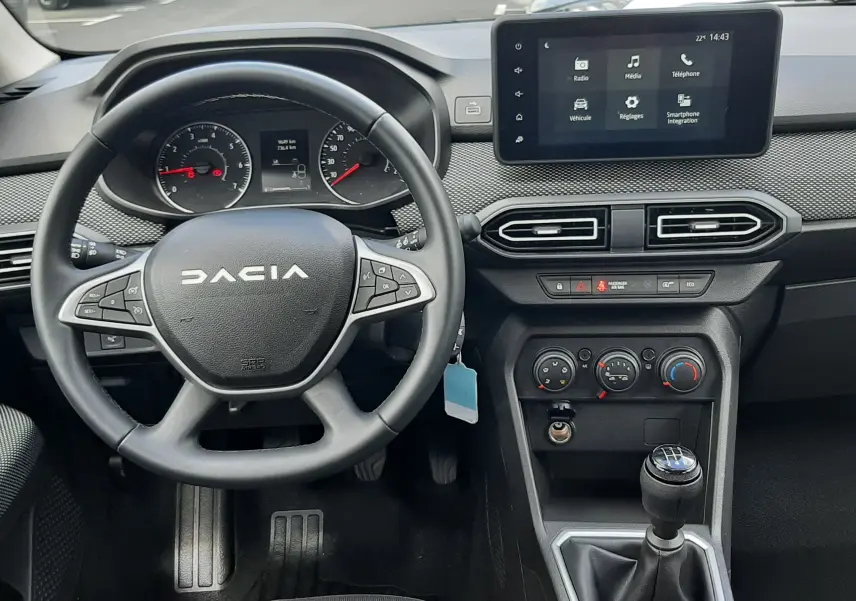 Vue intérieure du tableau de bord et volant noir de la Dacia Sandero 2024, avec écran tactile et levier de vitesses manuel.