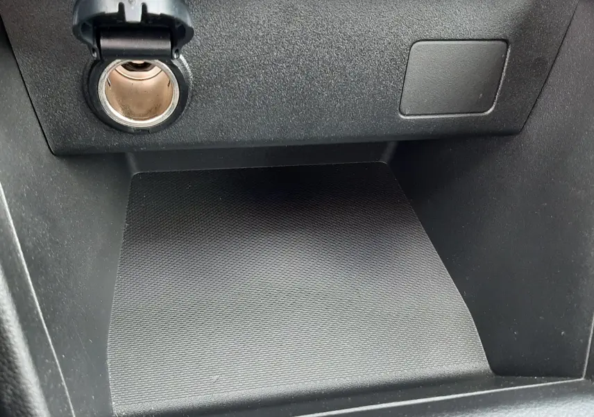 Gros plan sur la prise 12V et le rangement noir texturé du tableau de bord de la Dacia Sandero 2024.