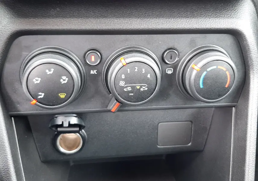 Vue rapprochée des commandes de climatisation manuelle noires du tableau de bord de la Dacia Sandero blanc glacier 2024.
