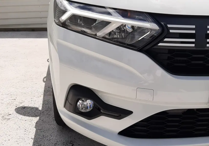 Gros plan sur l'avant droit blanc glacier d'une Dacia Sandero 2024, mettant en valeur le phare LED et la calandre noire.
