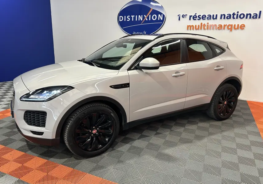Jaguar E-Pace beige vue 3/4 avant droit, jantes noires brillantes, toit panoramique et hayon électrique visibles.