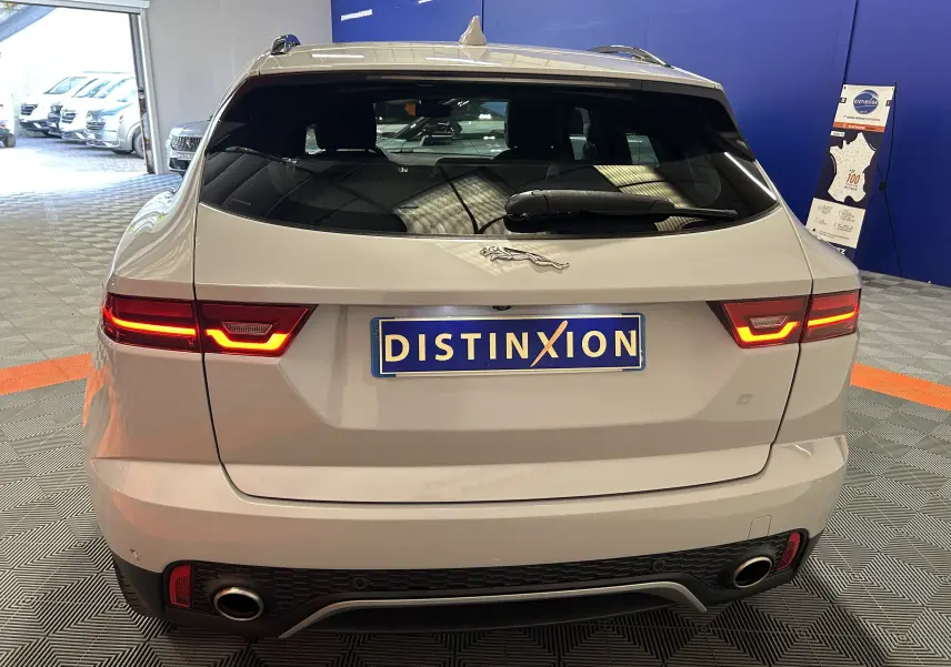 Vue arrière d'un Jaguar E-PACE beige 2018 avec feux allumés et hayon électrique dans un showroom intérieur.