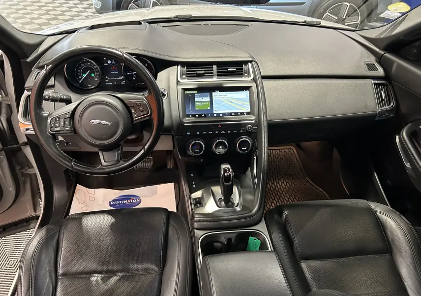 Vue intérieure avant du Jaguar E-PACE 2018 avec tableau de bord noir, volant cuir et écran tactile central allumé.