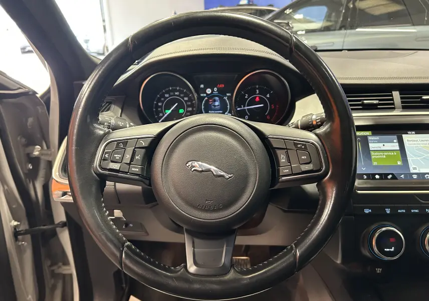 Vue intérieure centrée sur le volant cuir noir du Jaguar E-PACE beige, avec tableau de bord et écran tactile visibles.