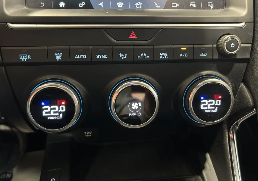 Gros plan sur les commandes de climatisation digitale du Jaguar E-PACE beige, affichant 22°C et fonctions activées.