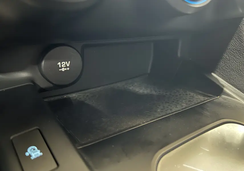 Détail de la prise 12V et du compartiment de rangement intérieur du Jaguar E-PACE beige, vue rapprochée côté console centrale.