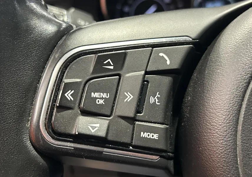 Gros plan sur les commandes multifonctions noires à gauche du volant du Jaguar E-PACE beige, boutons menu et téléphone visibles.