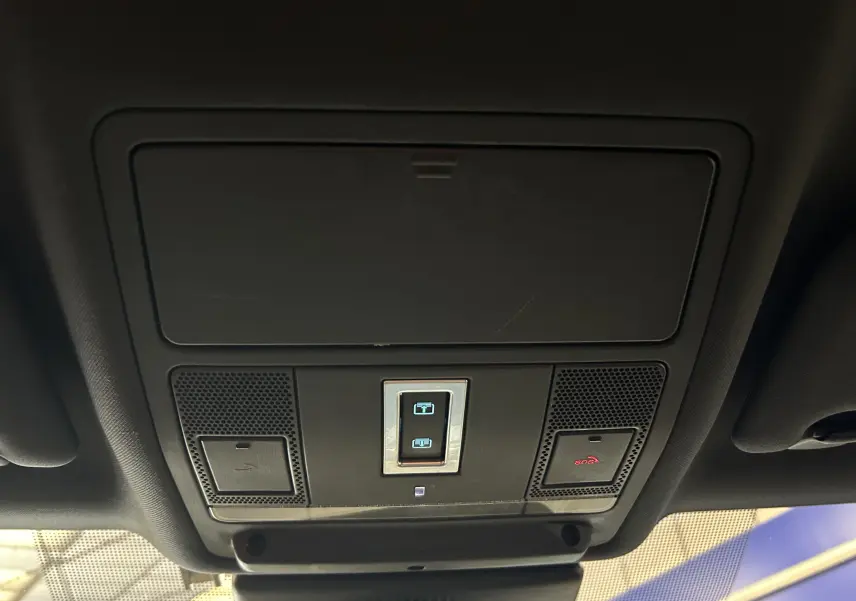 Vue en plongée sur le panneau de commande du toit panoramique et hayon électrique dans l'habitacle noir du Jaguar E-PACE beige.