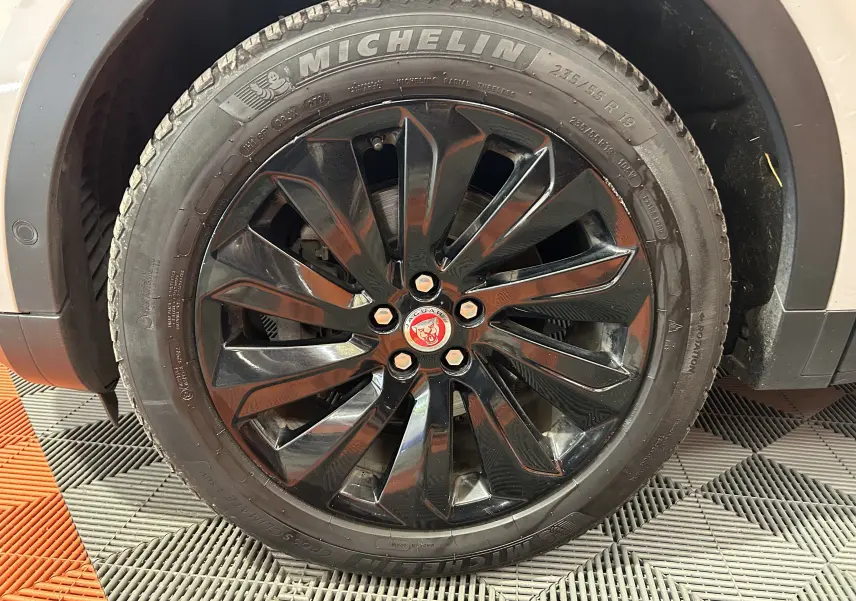 Gros plan sur la roue avant droite noire brillante du Jaguar E-PACE beige avec logo Jaguar rouge au centre.