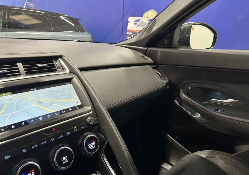 Vue intérieure côté passager du tableau de bord et de la porte d’une Jaguar E-Pace beige, avec écran tactile et climatisation digitale.