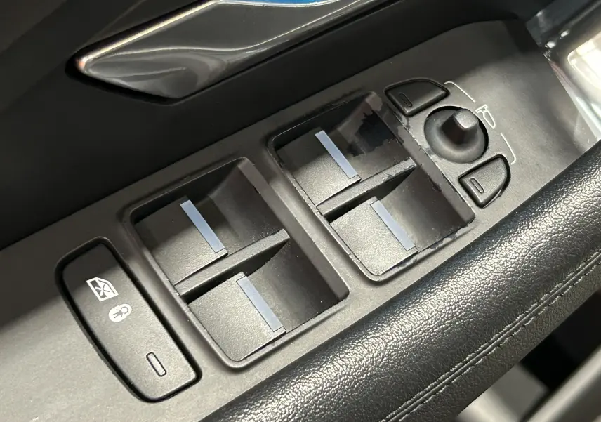 Gros plan sur les commandes de lève-vitres et rétroviseurs côté conducteur du Jaguar E-Pace beige de 2018.
