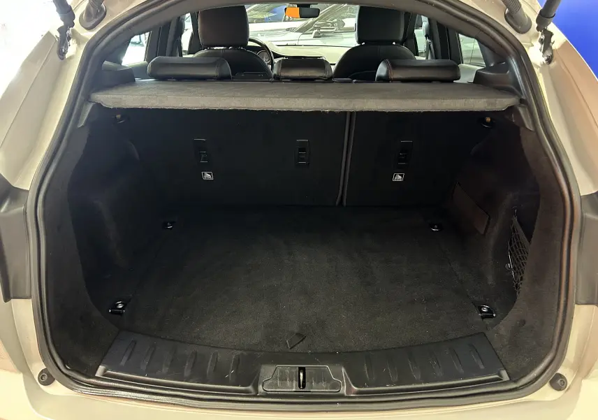 Coffre ouvert vu de l'arrière d'un Jaguar E-Pace beige, montrant un espace de chargement propre et bien agencé.