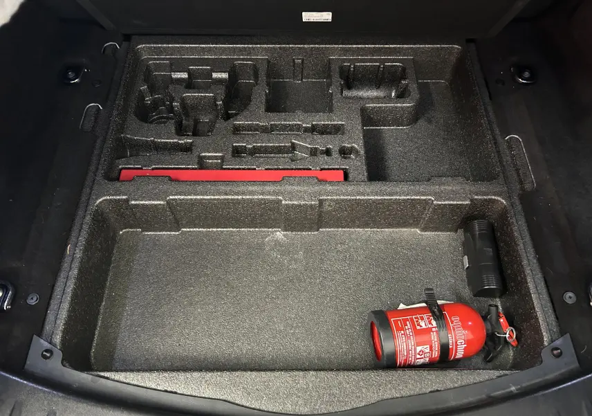 Coffre ouvert du Jaguar E-PACE beige 2018, vue plongeante sur compartiment de rangement avec extincteur rouge.